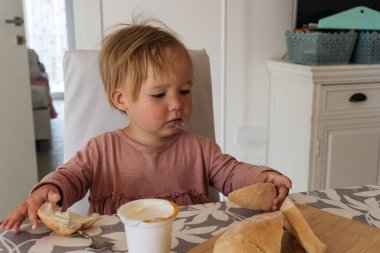 Small girl sitting at the table and having breakfast while looking into camera