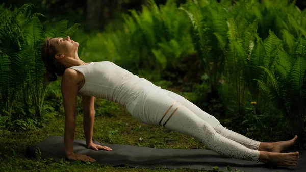 woman wearing white yoga suit practicing yoga in fern bushes. High quality photo