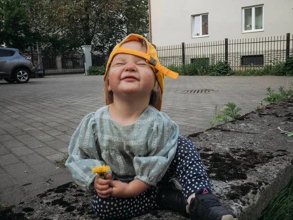 Baby girl in yBaby girl in yellow summer hat sitting in the backyard with dandelion. Shadow, copyspace