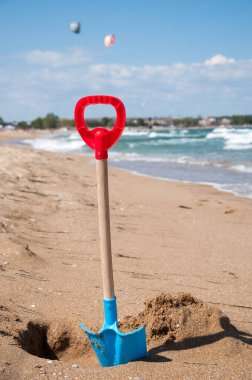 Çocukların mavi ve kırmızı küreği, kumsalda kumlara çakılmış.