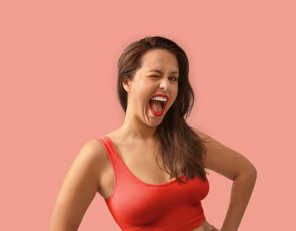 Happy young caucasian woman is winking to the camera. Medium shot in orange sport top on a seamless background. — Stock Photo, Image