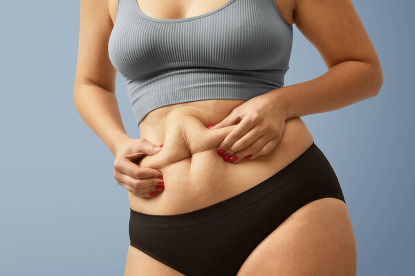 Upset plus size female on squeezing her abdomen excess fat. High quality studio photo image jpg