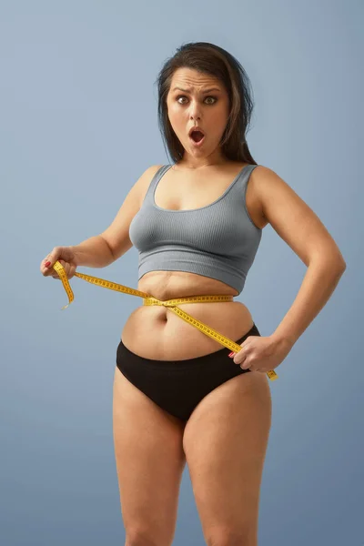 Sorprendido exceso de peso mujer caucásica envolver cinta métrica alrededor de su cintura. Imagen de foto de alta calidad. Fotos de stock libres de derechos