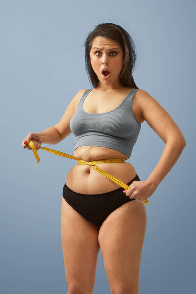 Surprised excess weight caucasian woman wrap measure tape around her waist. High quality photo image. Royalty Free Stock Photos