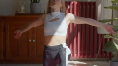 Formda, esnek, uzun saçlı, beyaz saçlı, yoga pozları veren ve evde duran bir kadın. Ön görüntü 4k video görüntüsü