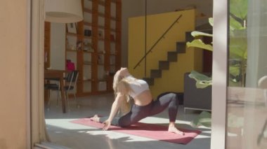 Formda, esnek sarışın, siyah spor sutyen giyen beyaz kadın ve yoga pozu veren taytlar ve evde ayakta duran kafa. 4k video kaydı