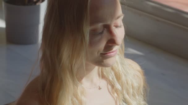 Mooie blonde blanke jonge vrouw maakt meditatie, opent ogen en draait het hoofd naar de camera. Videomateriaal nog steeds opgenomen portret. — Stockvideo