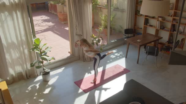 Cabello largo atractivo delgado mujer caucásica en un sujetador deportivo y leggins haciendo yoga posa en casa. Día soleado. Vista de arriba hacia abajo imágenes de vídeo 4k — Vídeo de stock