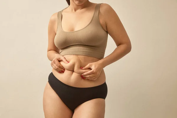 女性の体脂肪腹 肥満の女性の手に過剰なおなかの脂肪を保持します 健康的な胃の筋肉を形成するために食生活の概念を変更します 体の部分のスタジオ匿名のショットの写真 — ストック写真