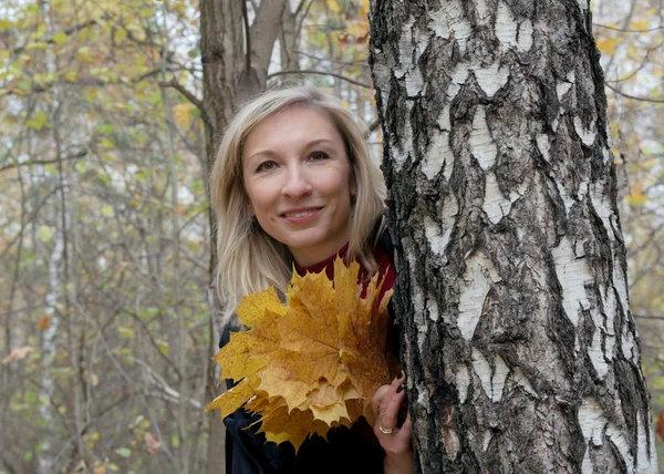 Lovely middle-aged woman with autumn leaves looking out from beh — Stockfoto