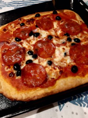 Domatesli, mozzarellalı, siyah zeytinli ve salamuralı ev yapımı pizzanın kesilip tadını çıkarmaya hazır bir görüntüsü. 