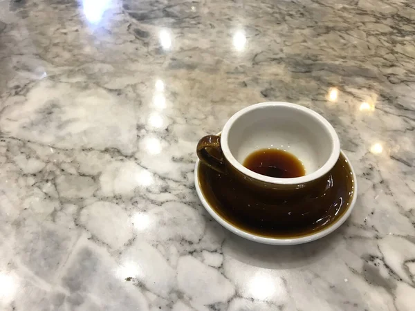 コーヒーショップの白と灰色の大理石のテーブルの上に置かれた電球と完成したアメリカの黒コーヒーの茶色のカップの暖かい反射 — ストック写真