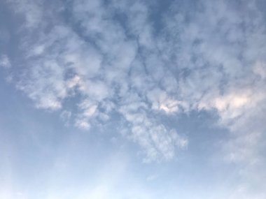 soluk mavi gökyüzü ve kabarık bulutlar pamuk gibi görünüyor çerçevenin sol alt köşesinde küçük parlak güneş ışığı ile