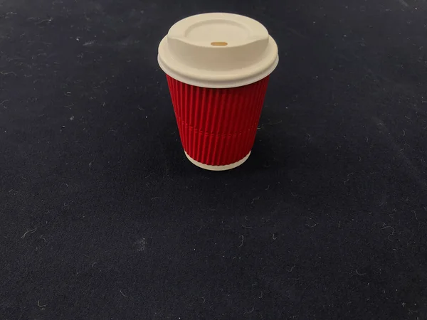 濃いネイビーブルーのテニスコートの真ん中にテニスボールの毛皮を入れたホットコーヒーの赤白の紙コップがあります — ストック写真