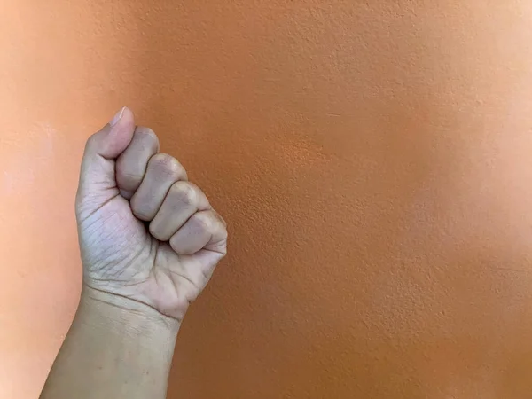 Arka planda soluk turuncu bir duvar olan bir adamın sol yumruğu, dövüş konsepti.