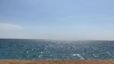Beyaz dalgalı ve parlak gün ışığında pürüzsüz kumsal sahili ile parıldayan mavi denizin solundan sağa sola dönen kameralı hareket