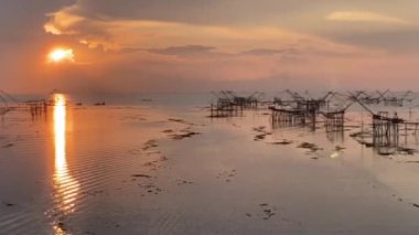 Büyük nehirde yükselen altın gün doğumu video çerçevesinin sağ tarafında bir sürü büyük balık tuzağı ağı var.