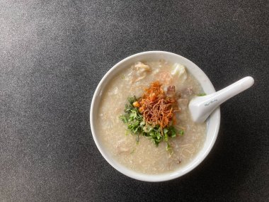 Bir kase pirinç lapası kıymalı, haşlanmış yumurta kızarmış soğan ve taze kişniş ve gri bir masaya konmuş beyaz porselen kaşık.