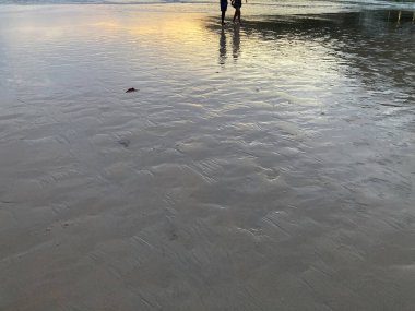 A loving couple is holding hands and strolling on the beach with a scene of the twilight sunset sky and silver sea waves