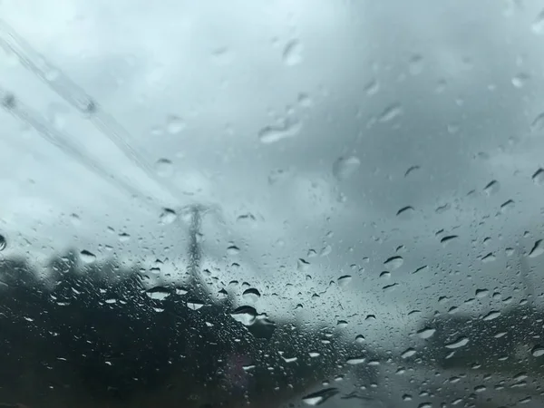 raindrops on the car's windscreen and blurred electric poles, trees, and gray stormy sky along the countryside road