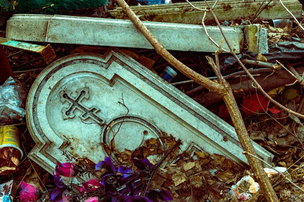 古い暗い墓石は乾燥した葉の山の中に人工の花の間にあり — ストック写真