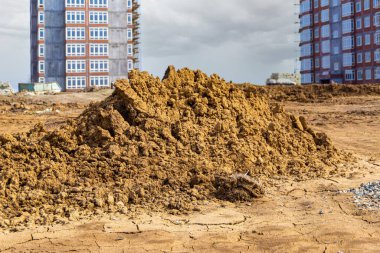 heaps of dry clay on construction site, preparation for landscaping, in background facade work on residential buildings