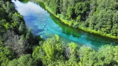 Bir grup insan rafting yapıyor. Bulutlar, nehrin ayna benzeri yüzeyine yansıyor.