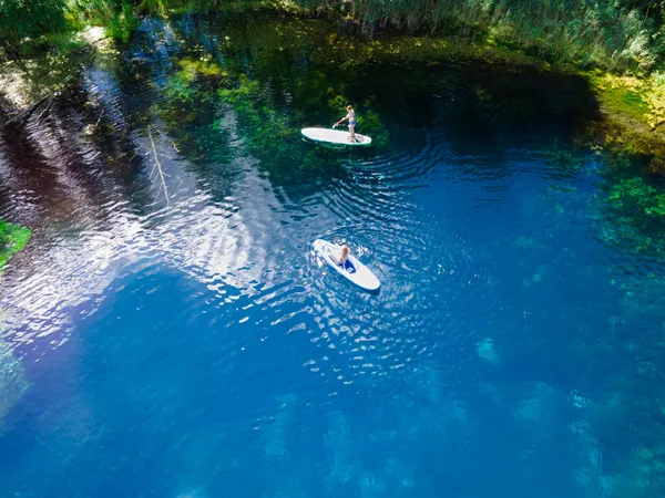Aşağısı berrak mavi sularda görülebilir. Ağaçlar ve güneş ışığı dalgaların yüzeyine yansıyor. Derin gölün kıyıları sazlıklar ve tırtıllarla kaplıdır..