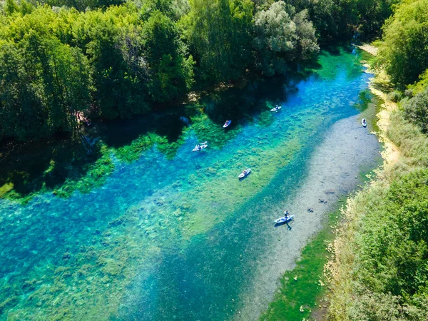 Korunan bölgedeki en saf orman gölü. Dokunulmamış vahşi doğanın güzelliği. Ağaçlar ve güneş ışığı suya yansıtılır. SUP üzerindeki tatilciler su yüzeyinde süzülüyor.