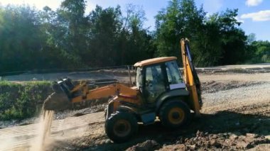 Sarı kepçe doldurucu yavaşça yukarı doğru sürüp yoldaki delikleri kumla kapatıyor.