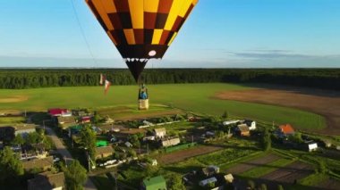 Two balloonists in gondola fly balloon. A yellow balloon over village at sunset. There is a place for the logo on the bag. The mood of freedom. A commercial balloon ride approaching its landing site