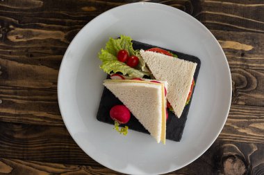 Beyaz tabakta ton balığı, marul ve domatesli sandviç.