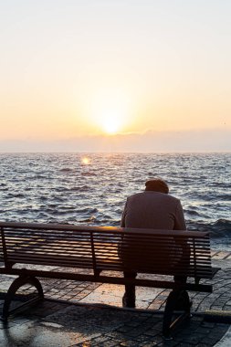 Adam gölün önündeki bankta tek başına oturuyor.