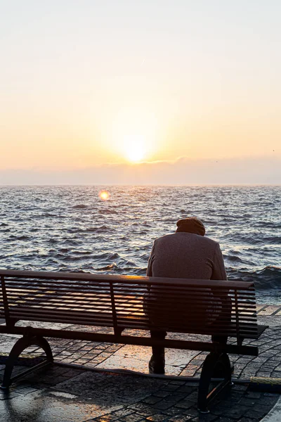 Adam gölün önündeki bankta tek başına oturuyor.