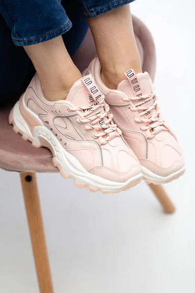 Female sneakers on legs. Pink woman\'s shoes on feet on chair. Sneakers close-up. Model in pink sneakers standing on chair