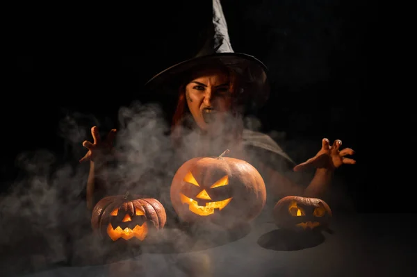 Zła wiedźma rzuciła zaklęcie na dynie. Portret kobiety w karnawałowym kostiumie halloween w ciemności — Zdjęcie stockowe