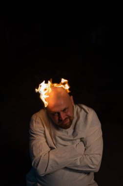 Kel bir adam, deli gömleği ve koyu bir arka planda yanan bir kafası var..