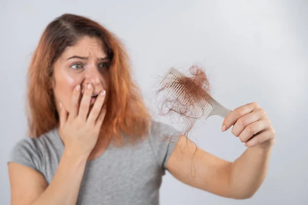 Λευκή γυναίκα με γκριμάτσα τρόμου κρατάει μια χτένα με μια τούφα μαλλιά. Τριχόπτωση και γυναικεία αλωπεκία. — Φωτογραφία Αρχείου