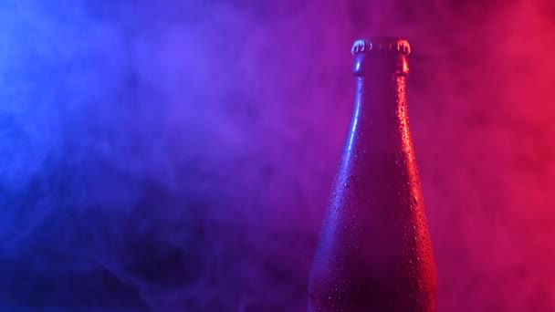 Pivní láhev se točí v modrém růžovém kouři. — Stock video