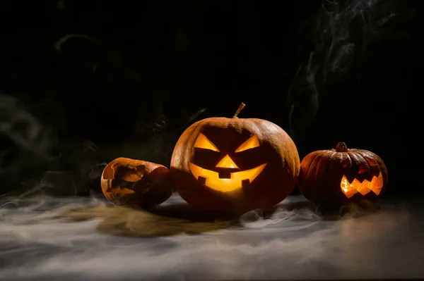 Dynie z rzeźbionymi grymasami i świecami wewnątrz w ciemności na Halloween. Jack o latern z dymem. — Zdjęcie stockowe