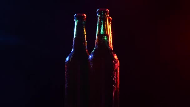 Tres botellas de cerveza girando en luz de color sobre un fondo negro. — Vídeo de stock