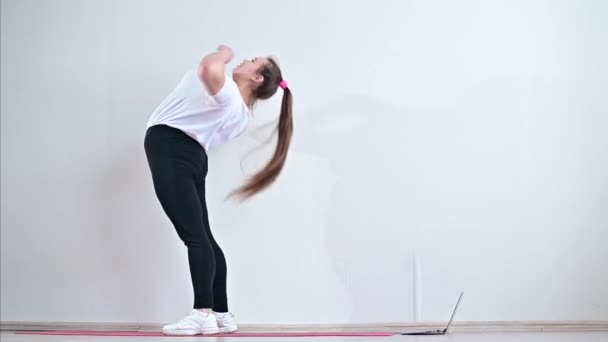 Mujer joven flexible se para en el puente y conduce una clase de gimnasia a distancia en un ordenador portátil. — Vídeos de Stock