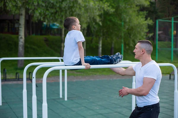 Caucasian man trains a boy on the uneven bars on the playground. Dad and son go in for outdoor sports.