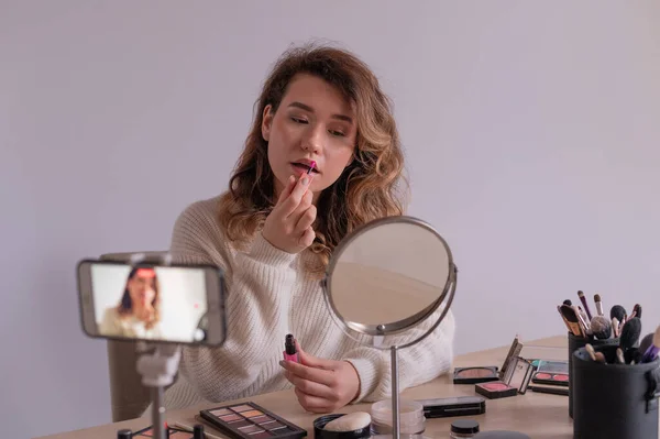 Mulher caucasiana jovem está gravando um vídeo de treinamento de maquiagem on-line em seu celular. Vídeo blogger girl aplica maquiagem. — Fotografia de Stock
