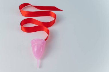 Pembe regl kupası ve beyaz arka planda kırmızı saten kurdele. Boşluğu kopyala