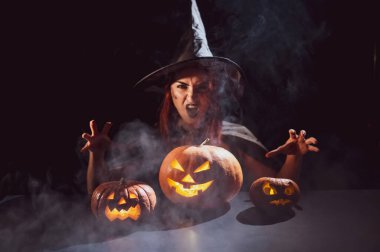 Kötü cadı balkabaklarına büyü yapıyor. Karanlıkta cadılar bayramı kostümü giymiş bir kadının portresi.