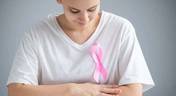 Mulher com um corte de cabelo loiro curto com uma fita rosa em uma camiseta branca como um símbolo de câncer de mama em um fundo branco. — Fotografia de Stock