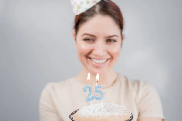 The happy woman makes a wish and blows out the candles on the 25th birthday cake. Girl celebrating birthday.