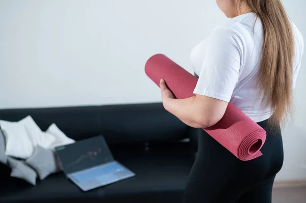 上完网上健身课后 胖胖的年轻女子会把运动垫叠起来 — 图库照片