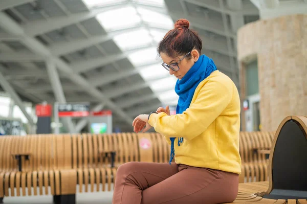 Mujer caucásica sentada en la estación de tren y mirando el reloj inteligente. —  Fotos de Stock